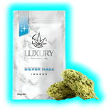 Nahaufnahme: Silver Haze Indoor (30g/40.-) in edler Verpackung mit Marmoroptik und zwei davor liegenden Blüten.