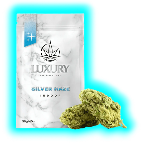 Nahaufnahme: Silver Haze Indoor (30g/40.-) in edler Verpackung mit Marmoroptik und zwei davor liegenden Blüten.