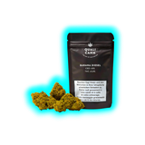 Schwarze Verpackung mit der Aufschrift 'QUALI CANN BANANA DIESEL CBD <18% THC <0,8%' neben mehreren Cannabisblüten.