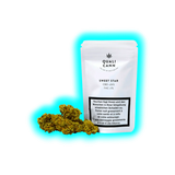 Weiße ‚Qualicann Sweet Star‘ Packung (<26% CBD, <1% THC) neben zwei getrockneten Cannabisblüten. Kompakte Detailansicht.